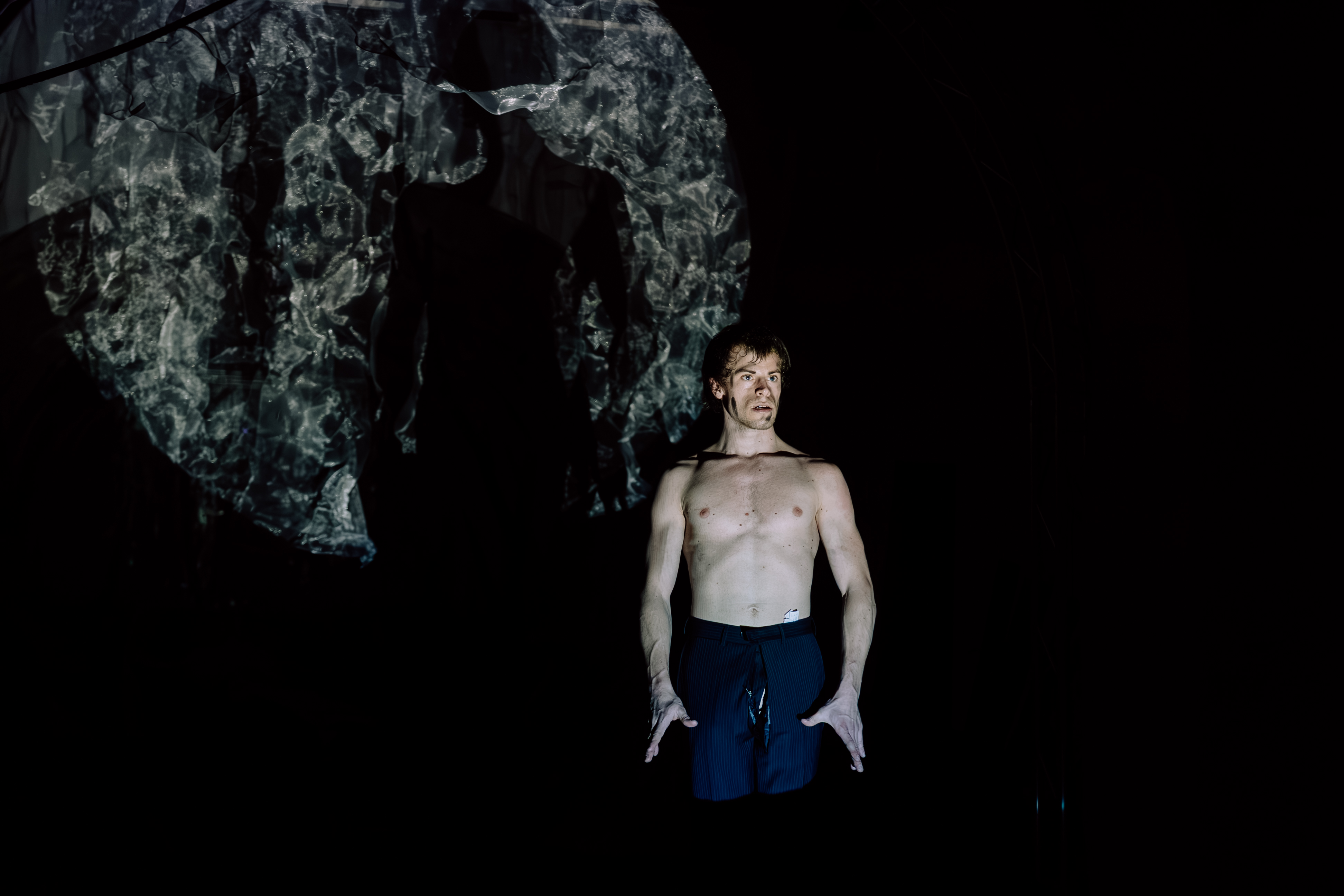 Nico Dorigatti performing in front of a projected figure in BROKE'N; an odd Messiah