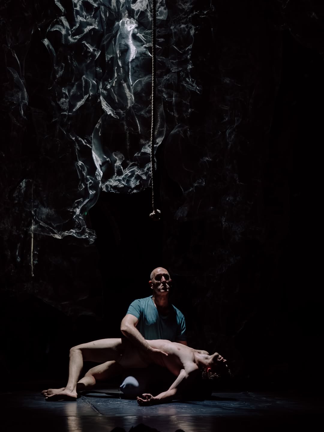 Two performers on a dark stage beneath a hanging rope in BROKE'N
